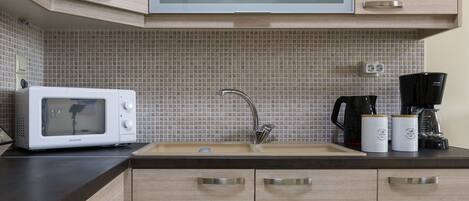 A kitchen with a microwave, sink, cabinets, and a coffee maker.