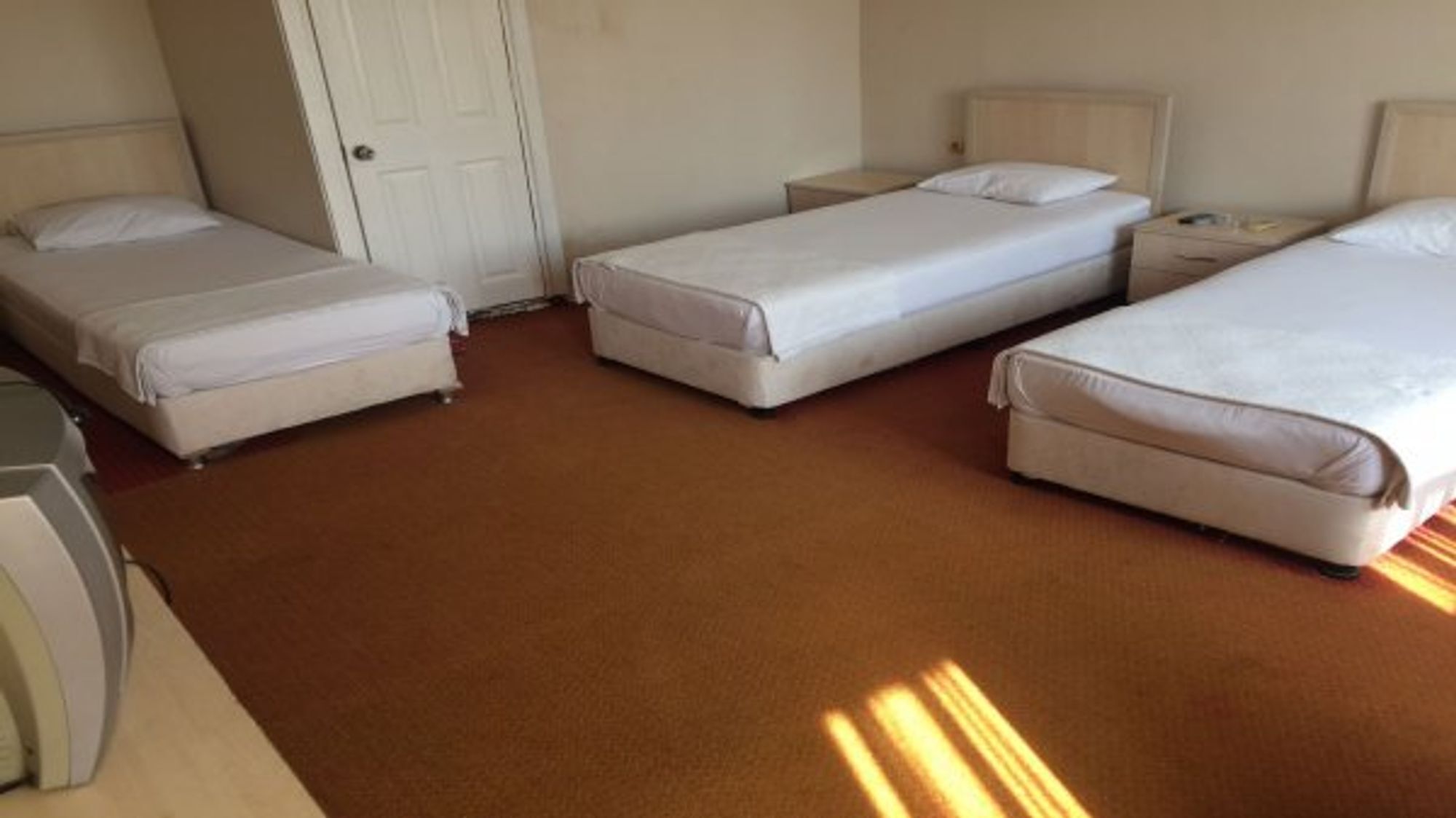 Een hotelkamer met drie eenpersoonsbedden, een bureau en een stoel.