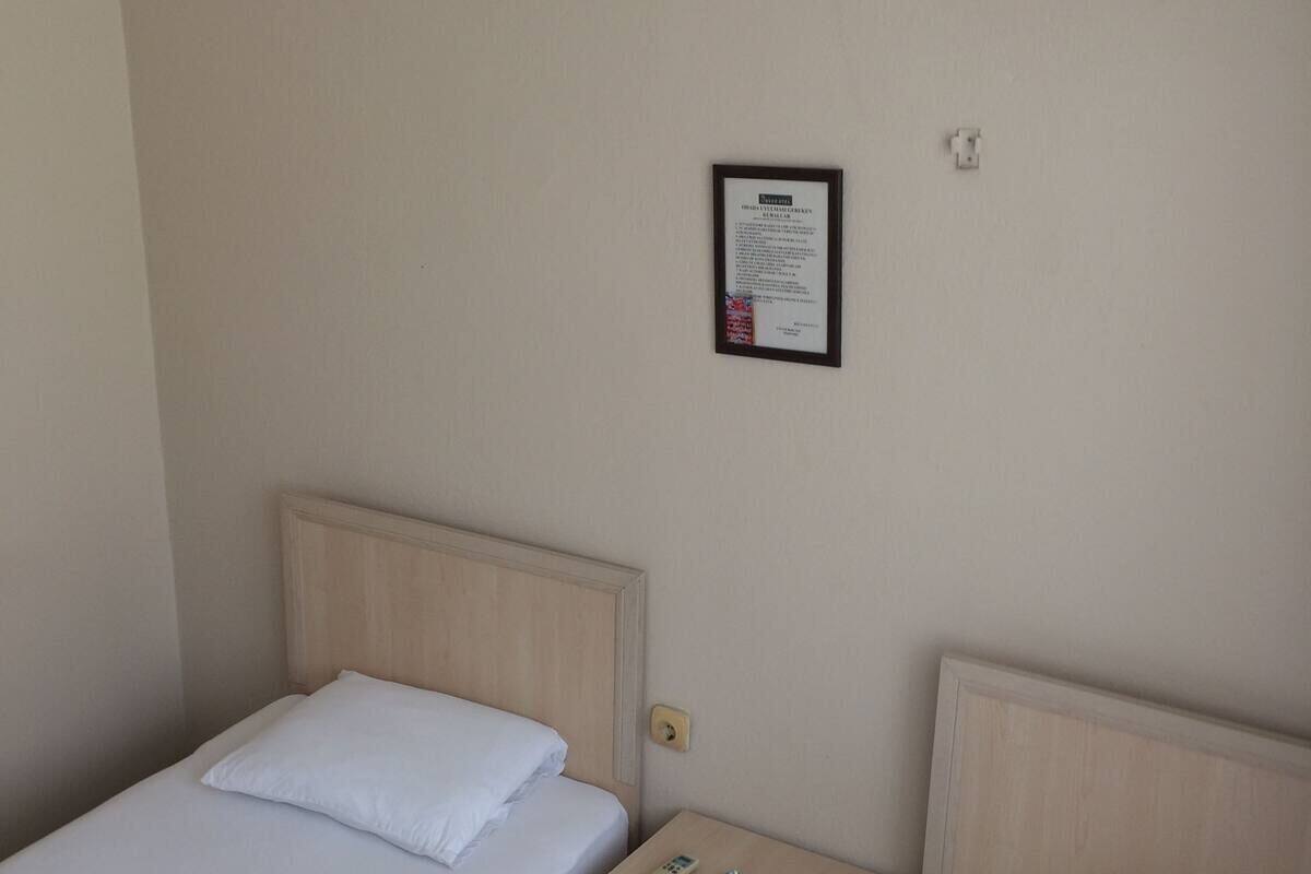 Una cama individual con cabecera de madera, una mesita de noche con un control remoto y un aviso en un marco en la pared.