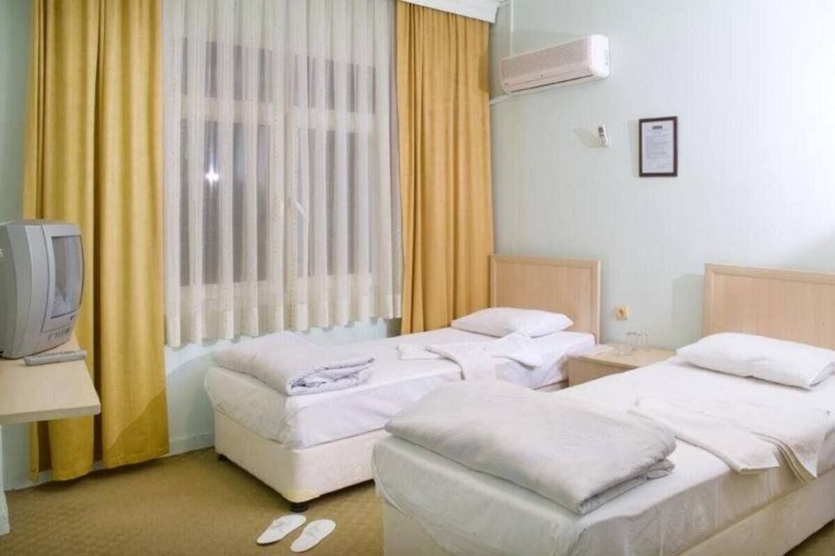 Habitación de hotel con dos camas, televisión y ventana con cortinas.