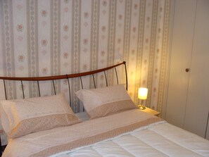 A bedroom with a bed, two pillows, a wooden headboard, a bedside lamp, and a wall with vertical stripes and floral patterns. - T4 near Hypercentre, private car box and loggia (Toulouse)
