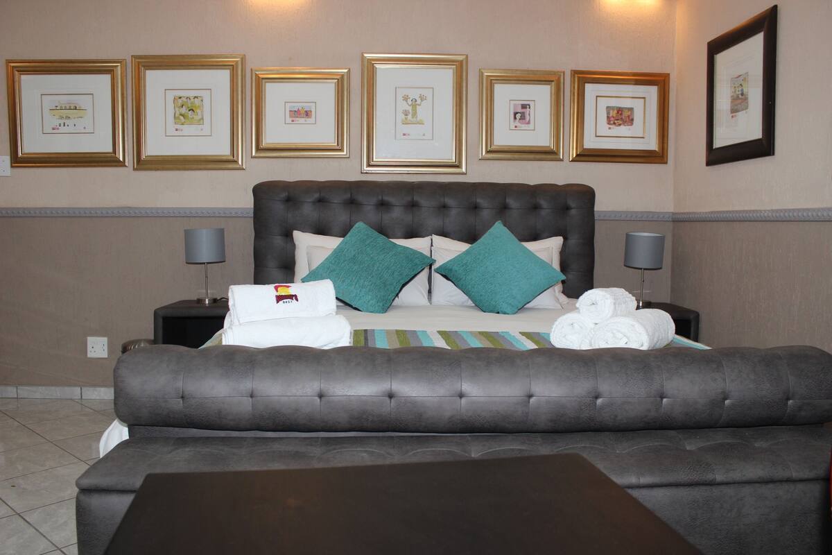 Une chambre d’hôtel avec un lit doté d’une tête de lit capitonnée, deux oreillers, une table de chevet avec une lampe et un canapé.