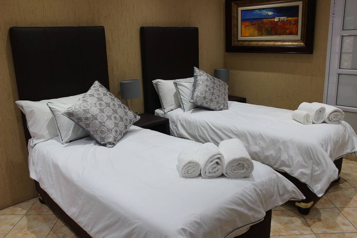 Une chambre d’hôtel avec deux lits, chacun étant équipé de draps blancs et d’oreillers à motifs. Des serviettes roulées sont posées sur les lits.