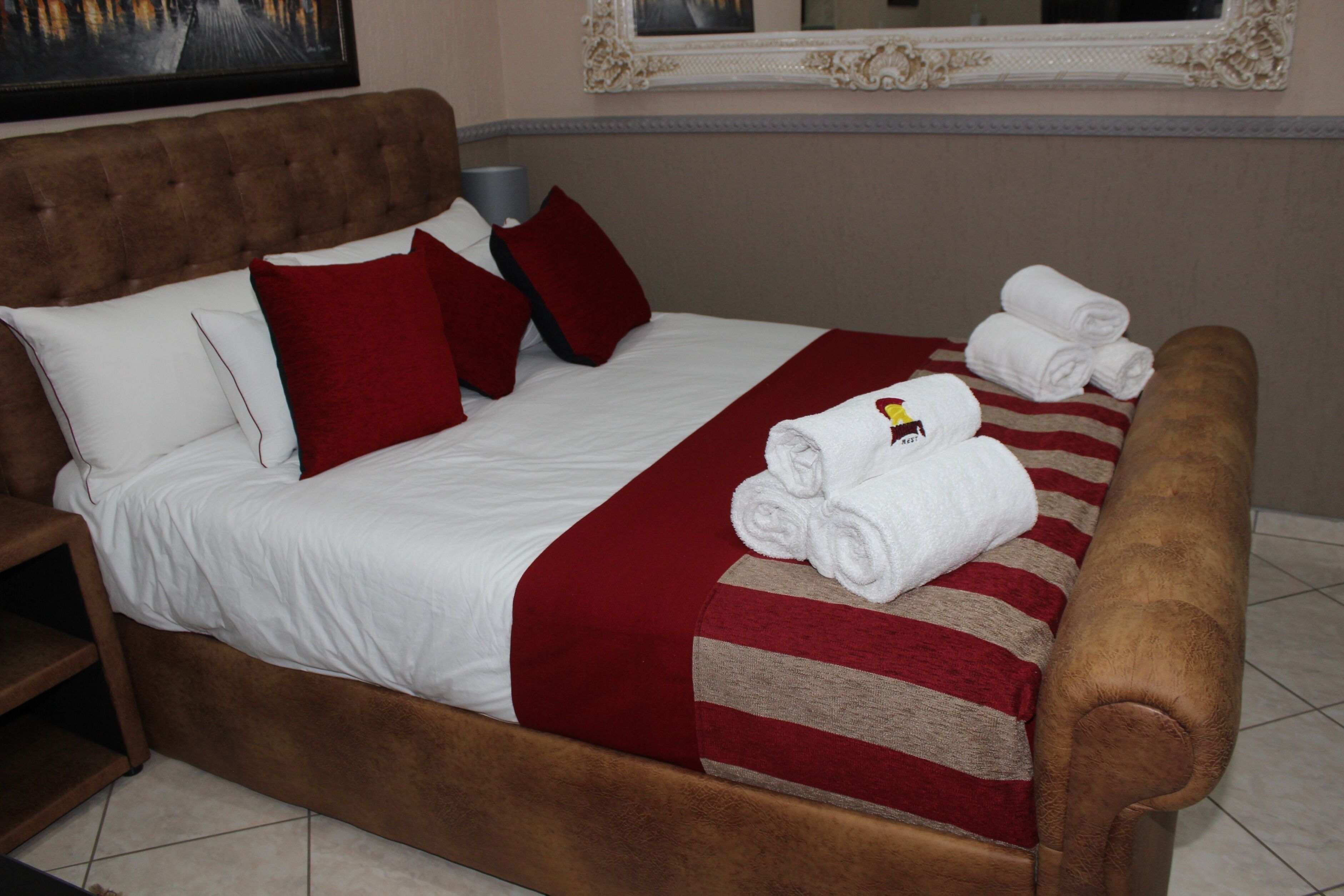 Uma cama bem arrumada com roupa de cama branca e vermelha, um cobertor listrado e toalhas dobradas.