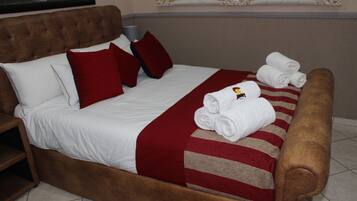 Uma cama bem arrumada com roupa de cama branca e vermelha, um cobertor listrado e toalhas dobradas.