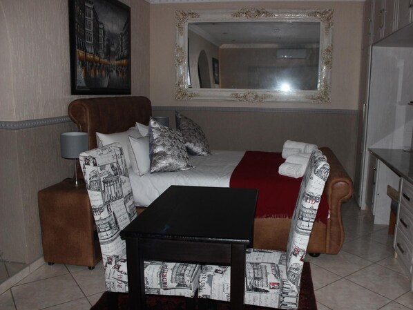 Une chambre d’hôtel avec un lit, une petite table, un canapé, un miroir et une lampe.