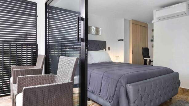 A modern bedroom with a bed, a chair, and a sliding glass door leading to a balcony. - 3 Bedroom Balcony, 3 Hot Tubs, AC (Medellin)