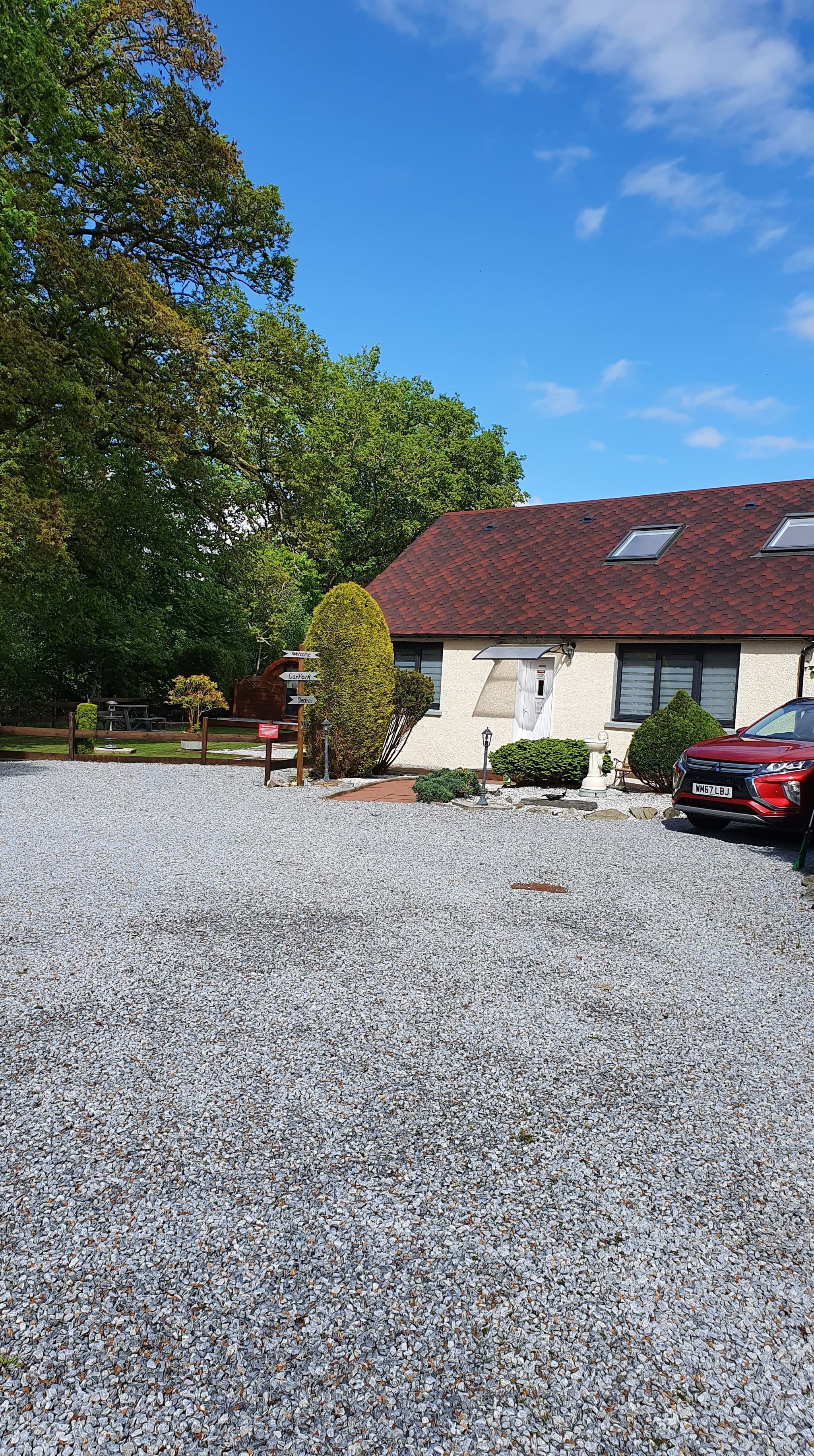 A building with a gravel driveway, a red car parked in front, and a sign indicating directions to 'Carpark' and 'Dine'.