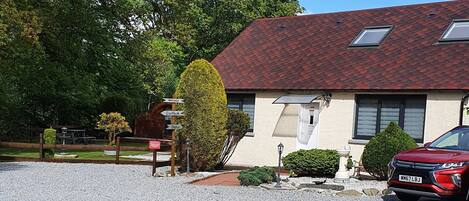 A building with a gravel driveway, a red car parked in front, and a sign indicating directions to 'Carpark' and 'Dine'.