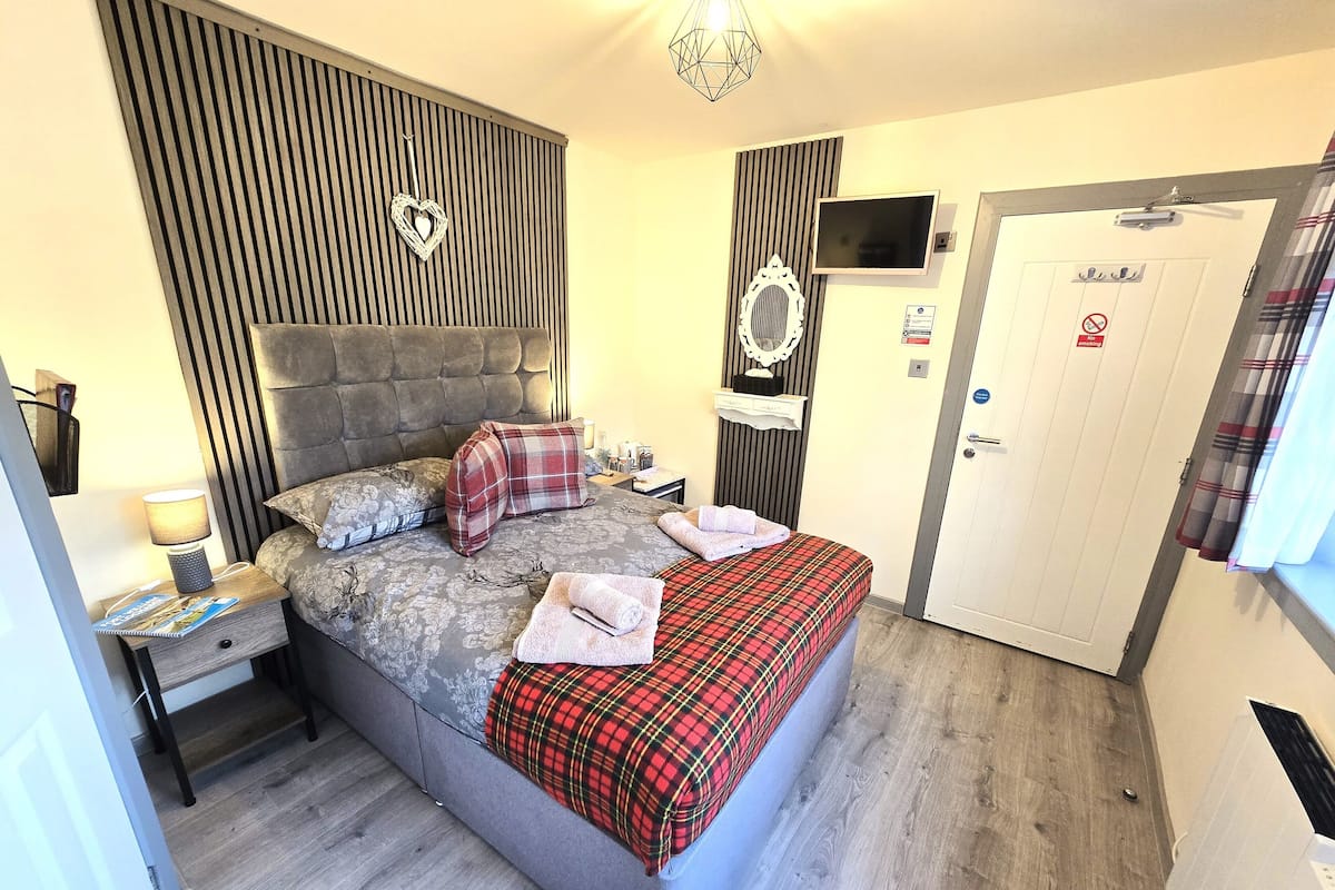 A neatly arranged bedroom with a bed, bedside tables, a TV, and a door with a no-smoking sign.
