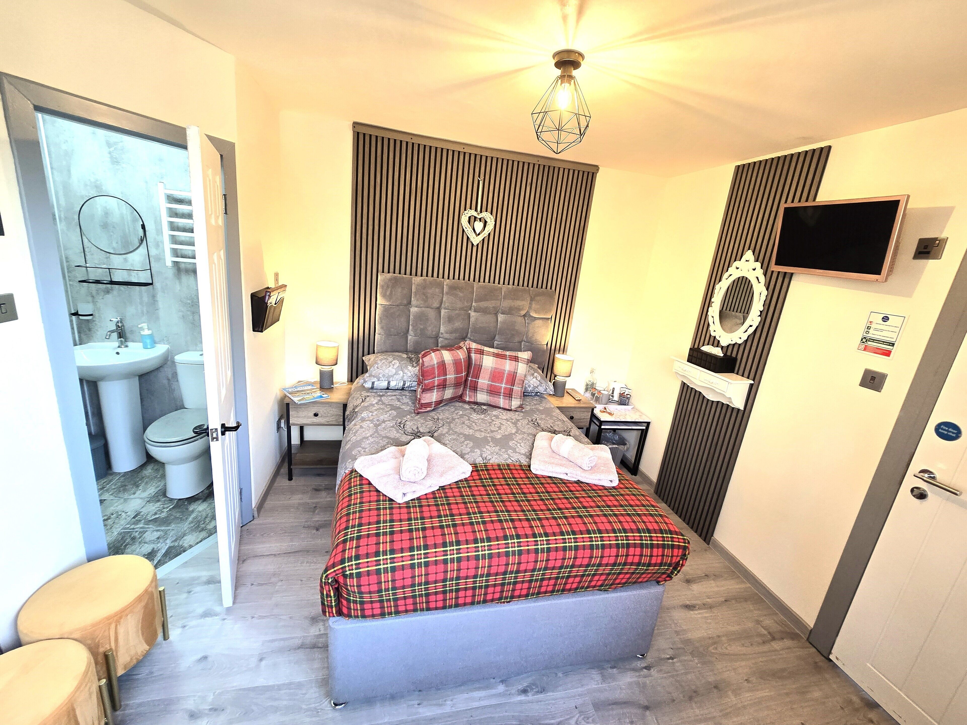 A bedroom with a bed, bedside tables, a TV, a mirror, and a bathroom with a sink and toilet.