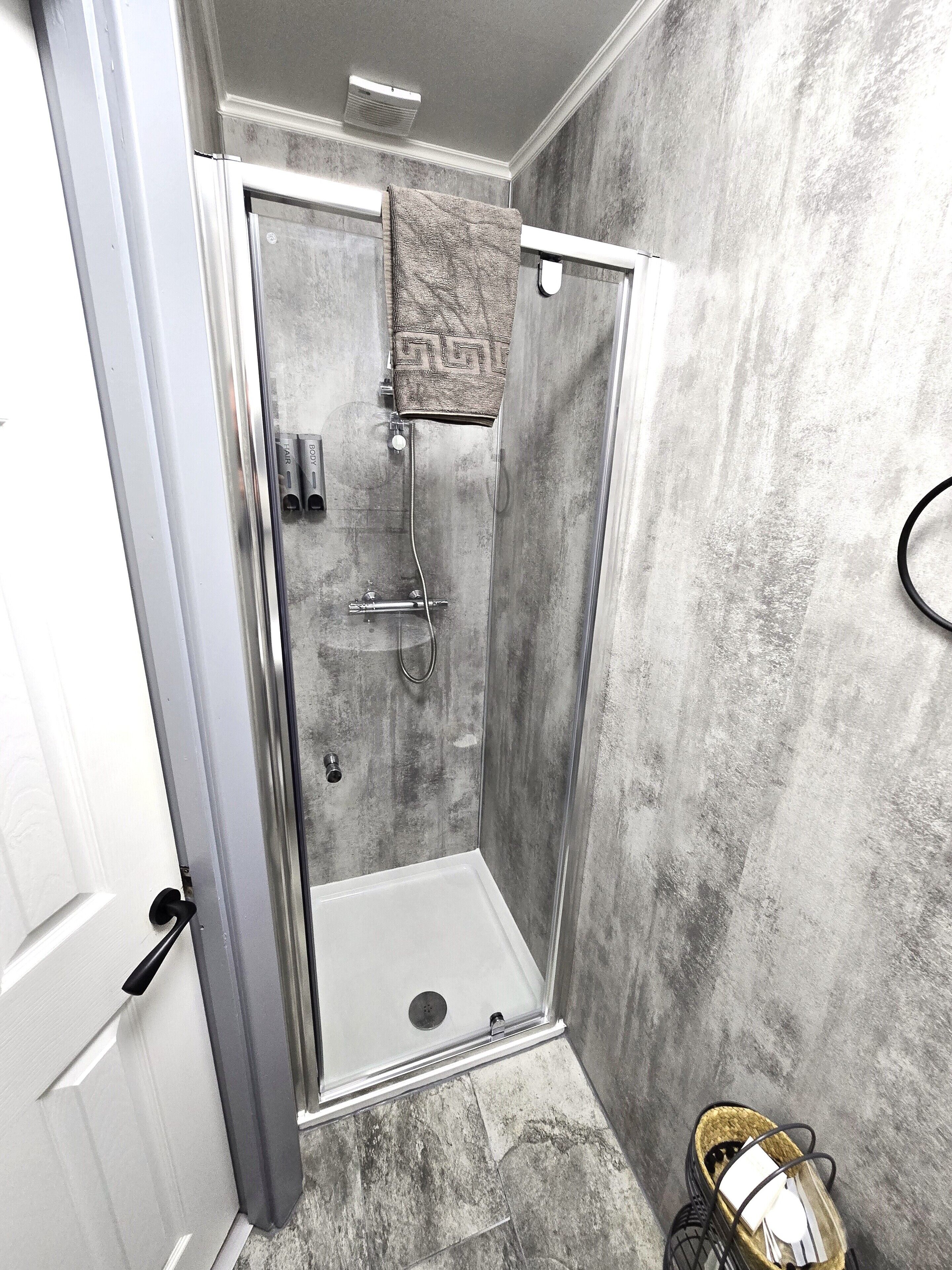 Un espace douche doté d’une porte en verre, une serviette accrochée au mur et un pommeau de douche.