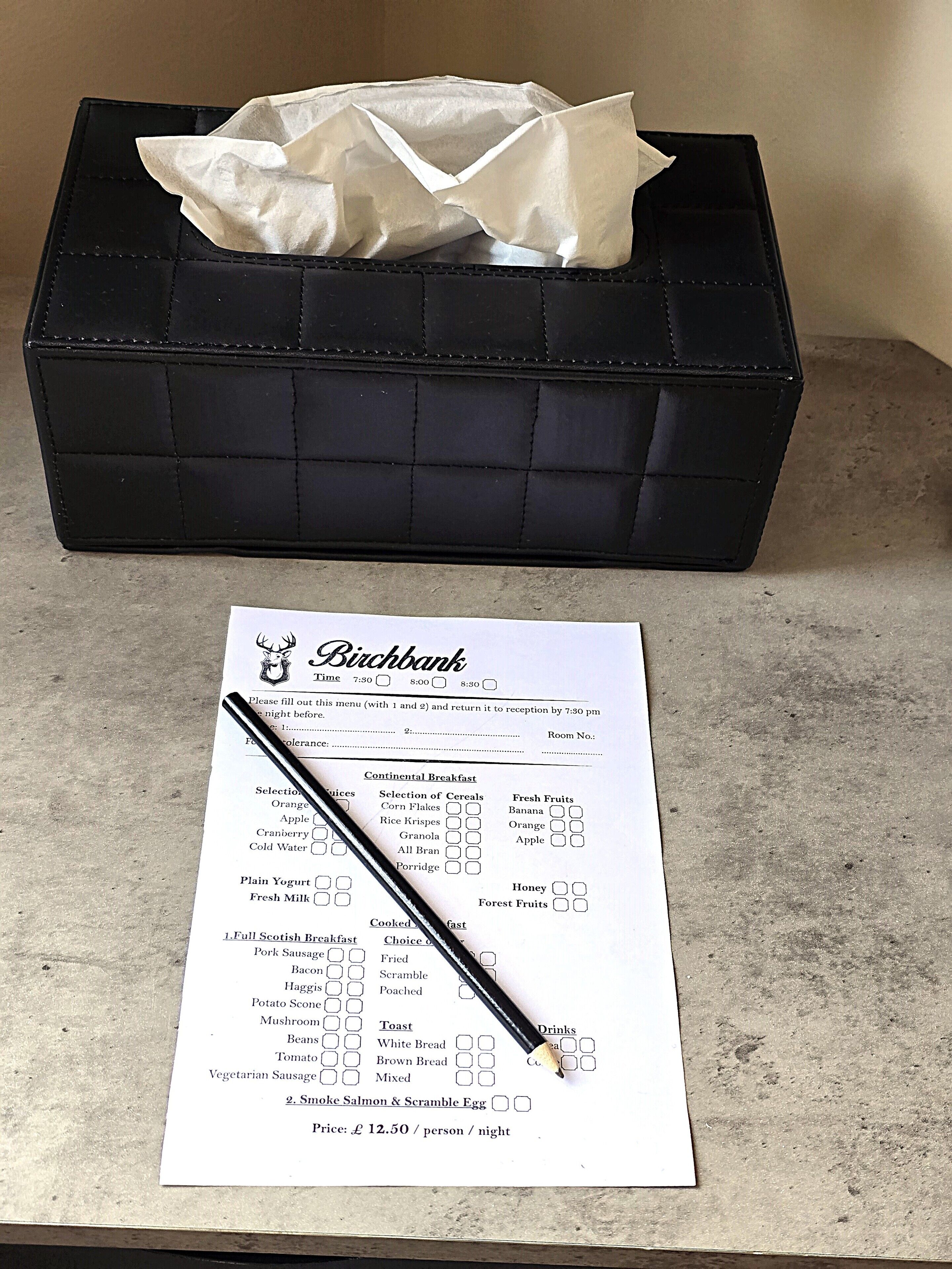 A menu with a black pen on it, placed on a table next to a black box with a tissue inside.