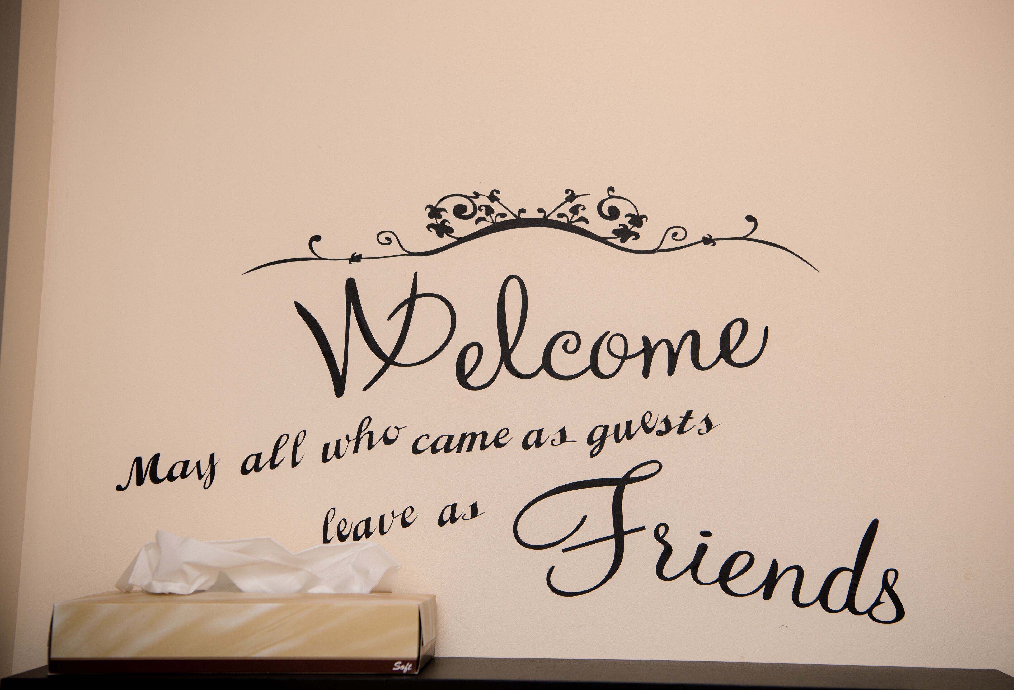 A wall with a decorative sign that reads "Welcome May all who came as guests leave as Friends."