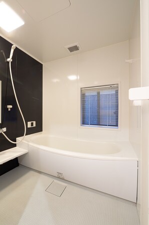 A modern bathroom with a large bathtub, a window with blinds, and a showerhead.