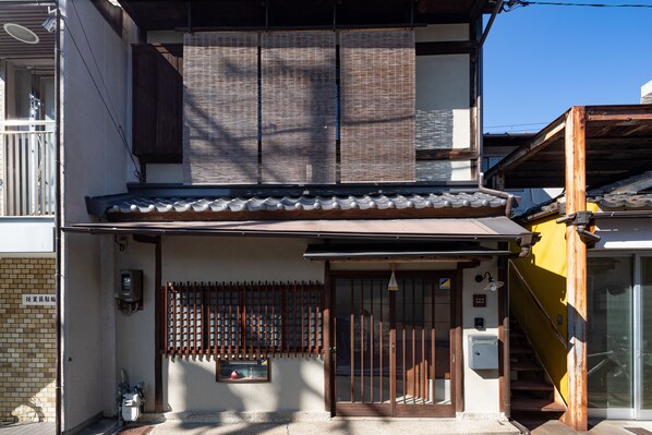 A traditional Japanese house with a tiled roof, a wooden gate, and a small window.