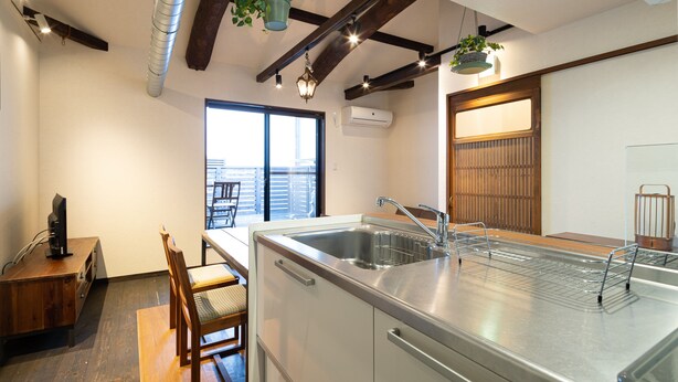 A modern kitchen with a large island, wooden dining table, and chairs. There is a window with a view of the outside. - Jishoan (Kyoto)