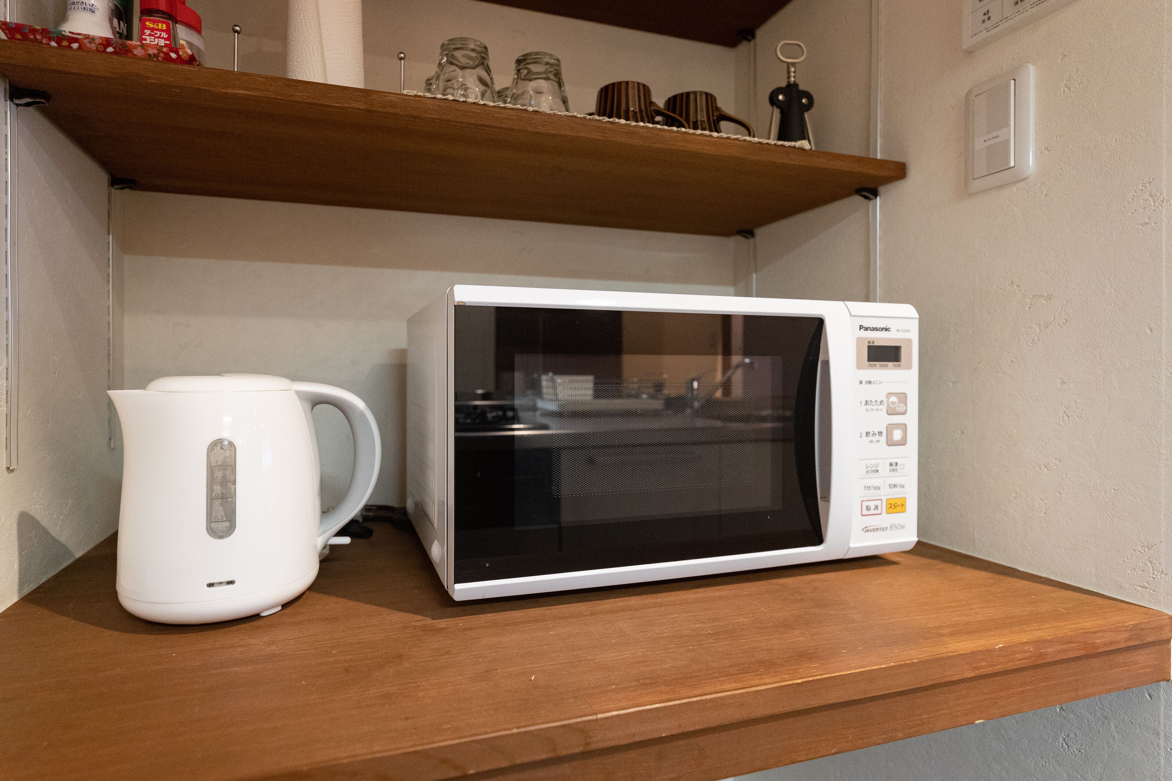 Een magnetron en een witte elektrische waterkoker op een houten plank.