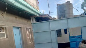 A narrow alleyway with a blue door, a blue structure, and a large water tank in the background. - Aberdare Guest House (Naivasha)