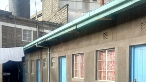 A building with a concrete exterior, multiple blue doors, and windows with metal grilles. - Aberdare Guest House (Naivasha)