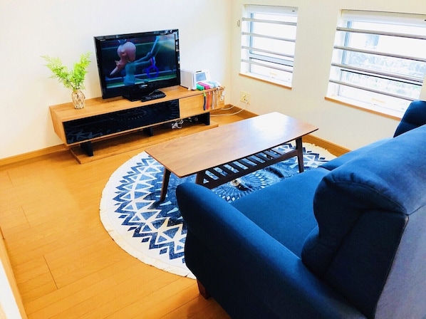 A living room with a flat-screen TV on a wooden stand, a coffee table, a blue sofa, and a patterned rug.