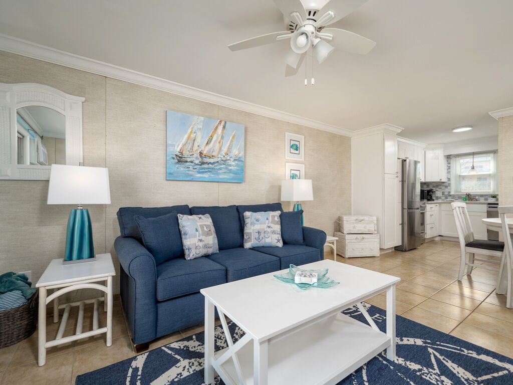 A living room with a blue sofa, white coffee table, and a painting of sailboats.