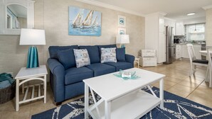 A living room with a blue sofa, white coffee table, and a painting of sailboats.