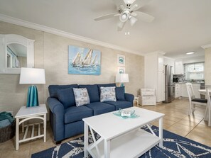 A living room with a blue sofa, white coffee table, and a painting of sailboats.