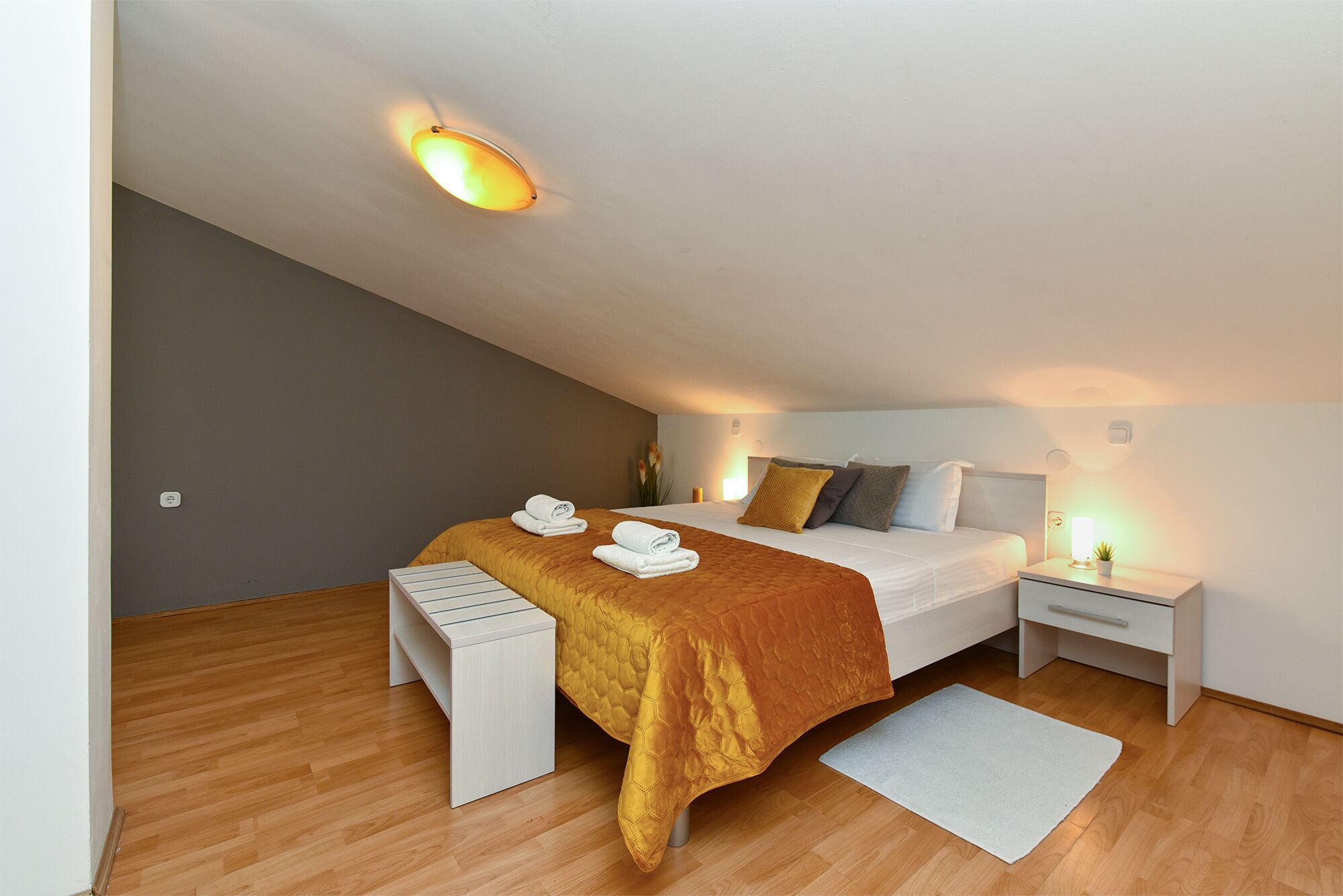 A modern bedroom with a bed, bedside tables, a bench, and a small rug.
