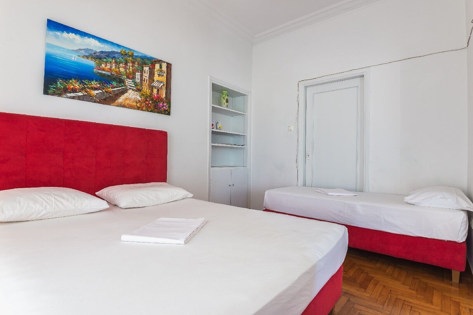 Une chambre d’hôtel avec un grand lit, un plus petit lit, une armoire et une étagère contenant des articles de toilette.