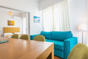 A room with a wooden dining table, a blue sofa, and a bed with a yellow headboard.