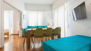 Una habitación compacta con una mesa de comedor, sillas, un sofá y un televisor montado en la pared.