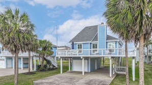 Une propriété située en bord de mer, avec un bâtiment bleu, une terrasse couverte et un escalier menant à un deuxième étage.