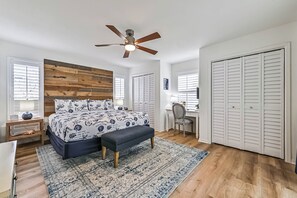 Une chambre à coucher avec une tête de lit en bois, un lit avec une literie à motifs, un ventilateur de plafond, un bureau avec une chaise et une armoire.