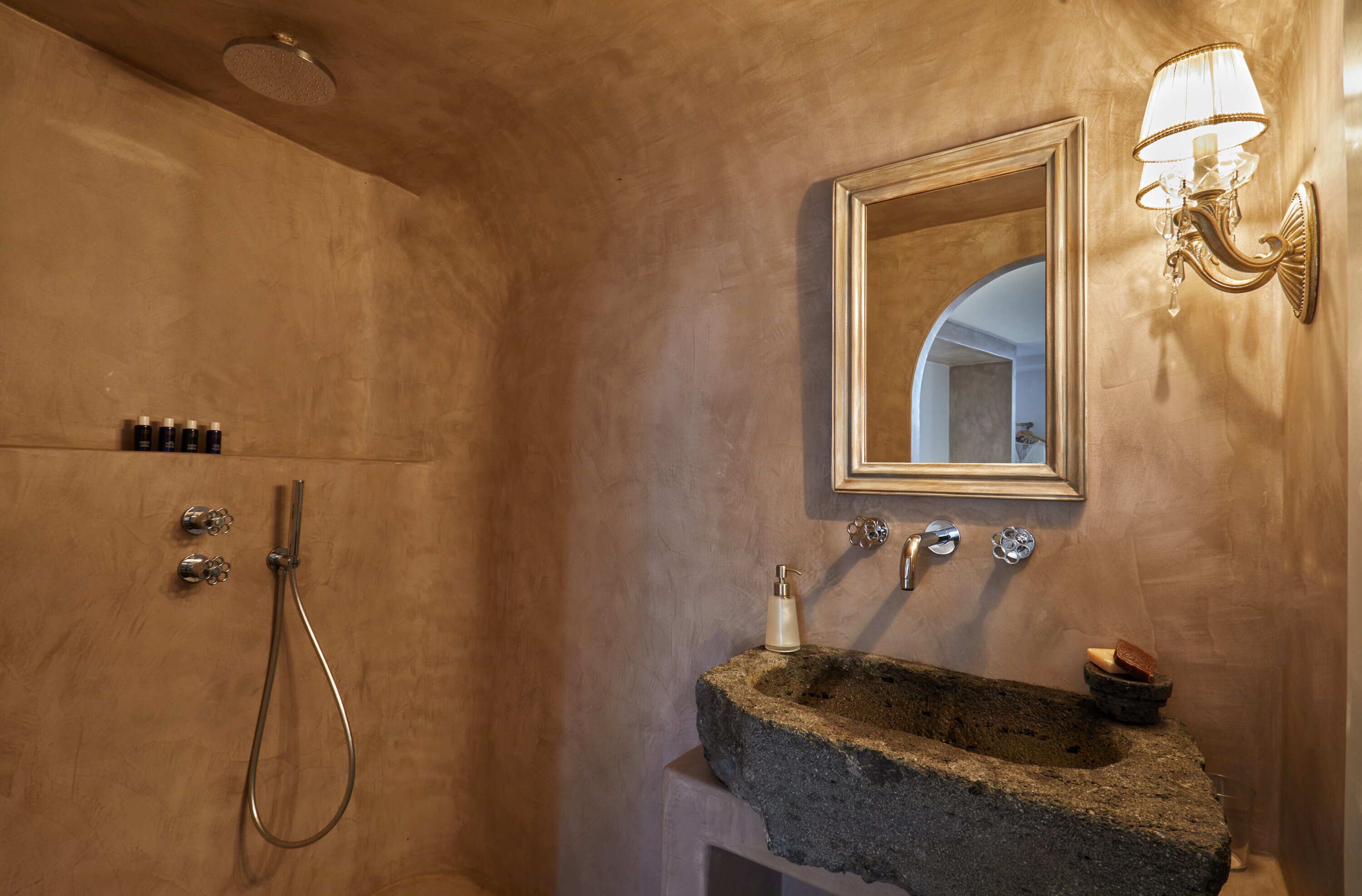 A bathroom with a stone sink, a mirror, and a shower with a handheld showerhead.