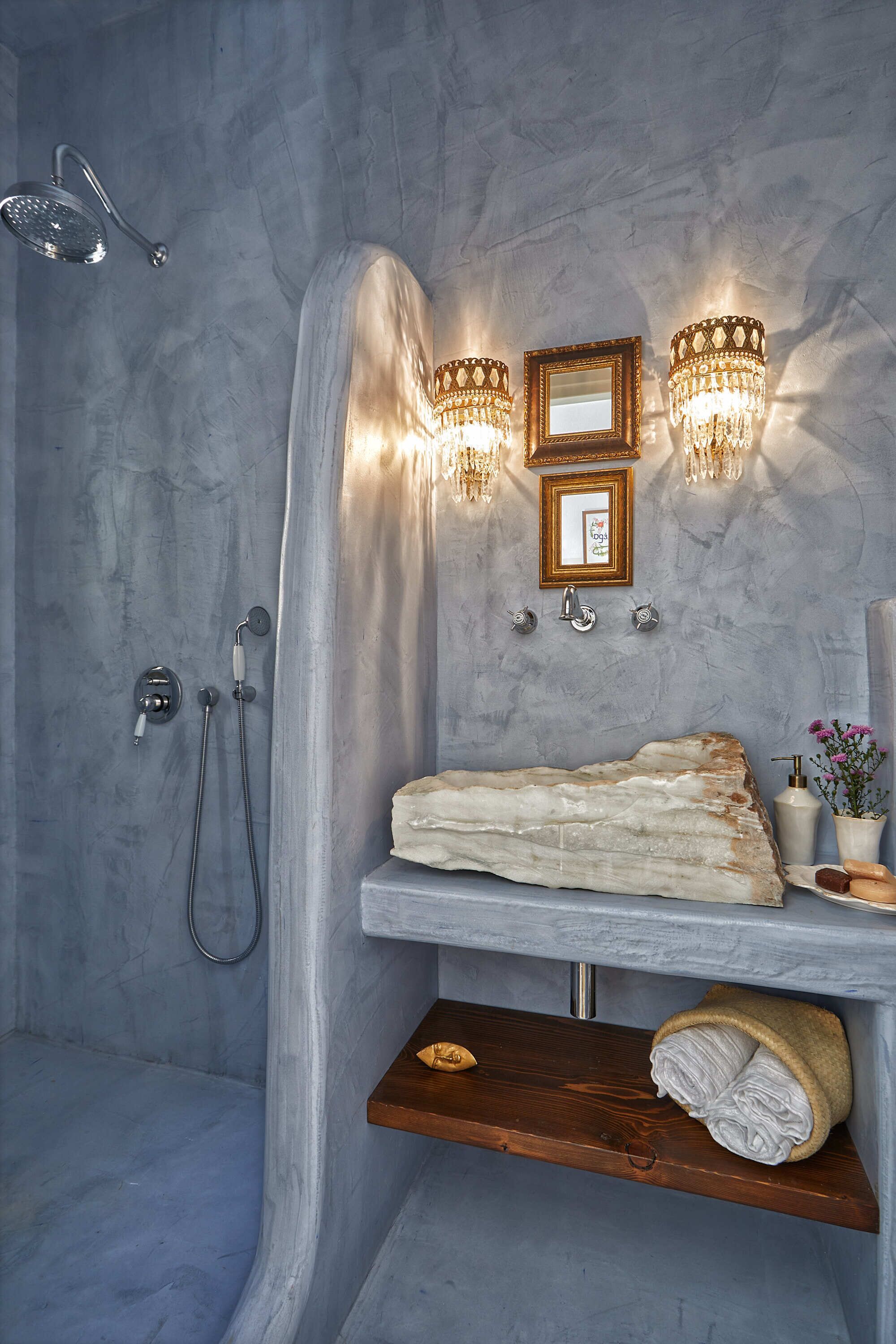A bathroom with a stone sink, wooden shelf, and a shower with a curved wall.