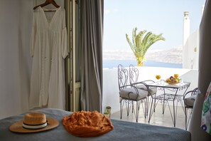 A balcony with a table set for two, a hanging dress, and a hat on a bed. - Arvanitis Cave Village (Santorini)