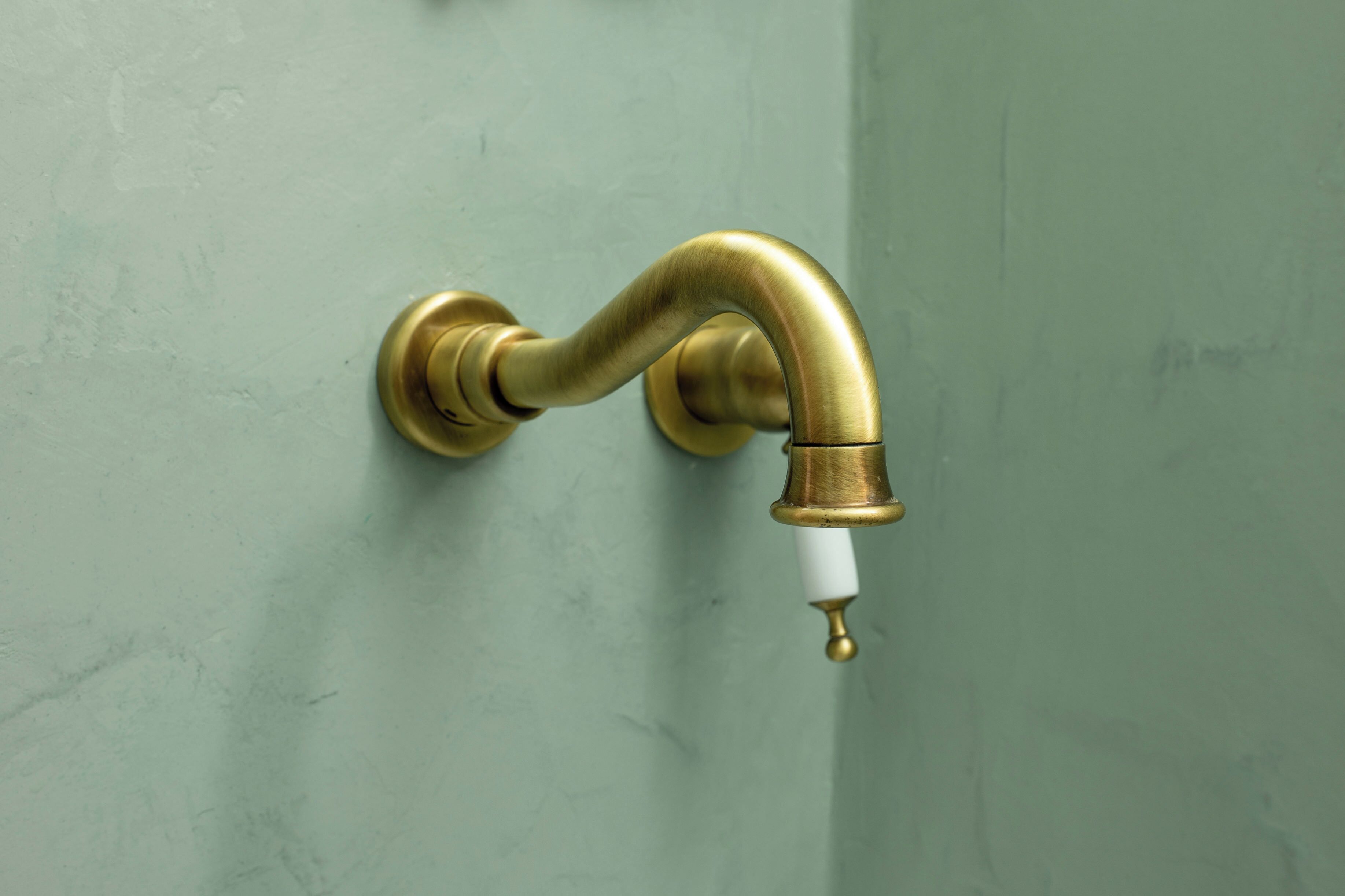 A brass faucet with a white handle attached to a green wall.