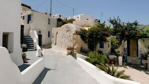 A narrow, white-walled street with steps leading to a building entrance, surrounded by potted plants and a clear blue sky. - Arvanitis Cave Village (Santorini)