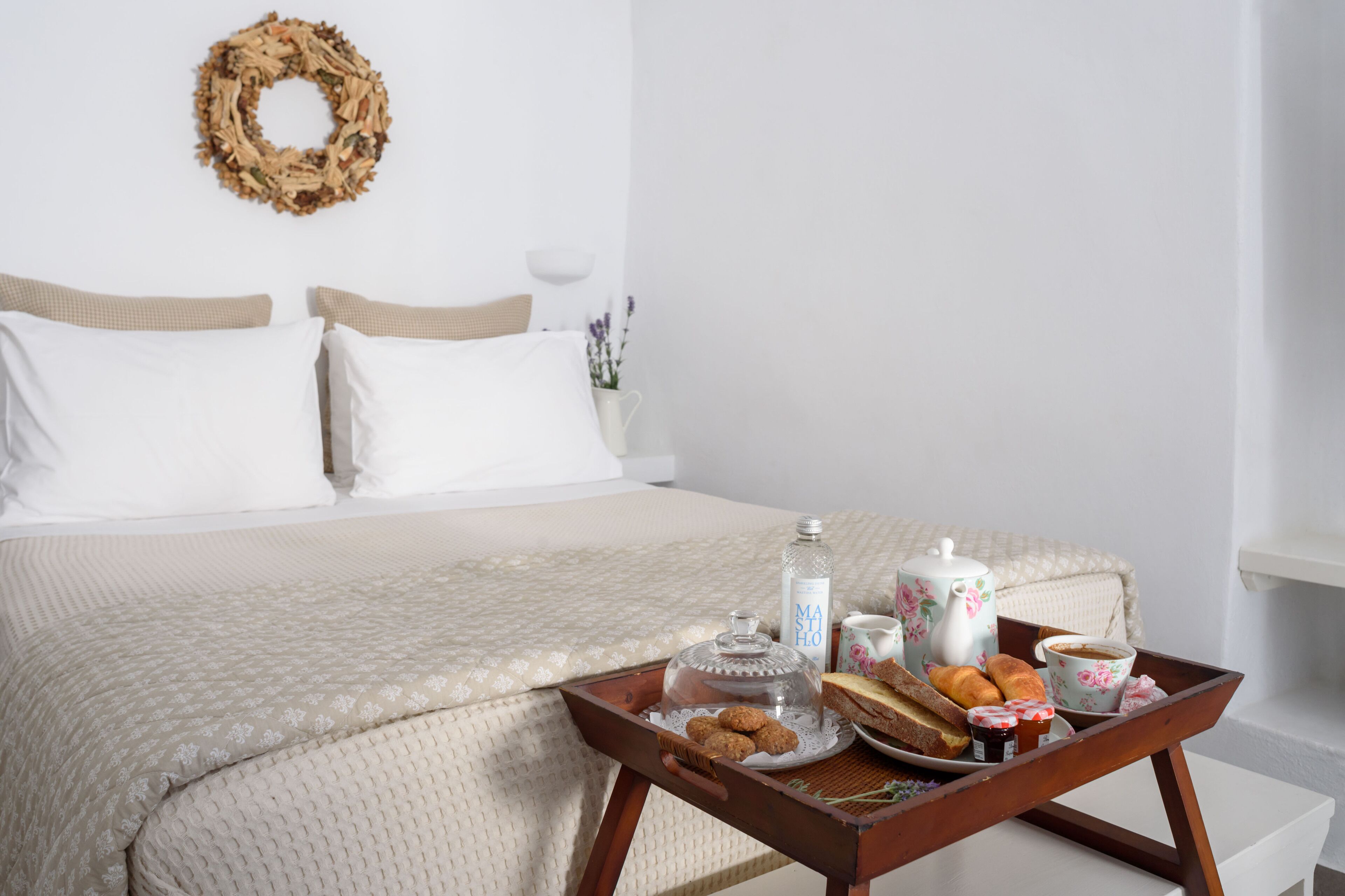 A neatly made bed with a beige quilt, a tray with breakfast items, and a floral wreath on the wall.