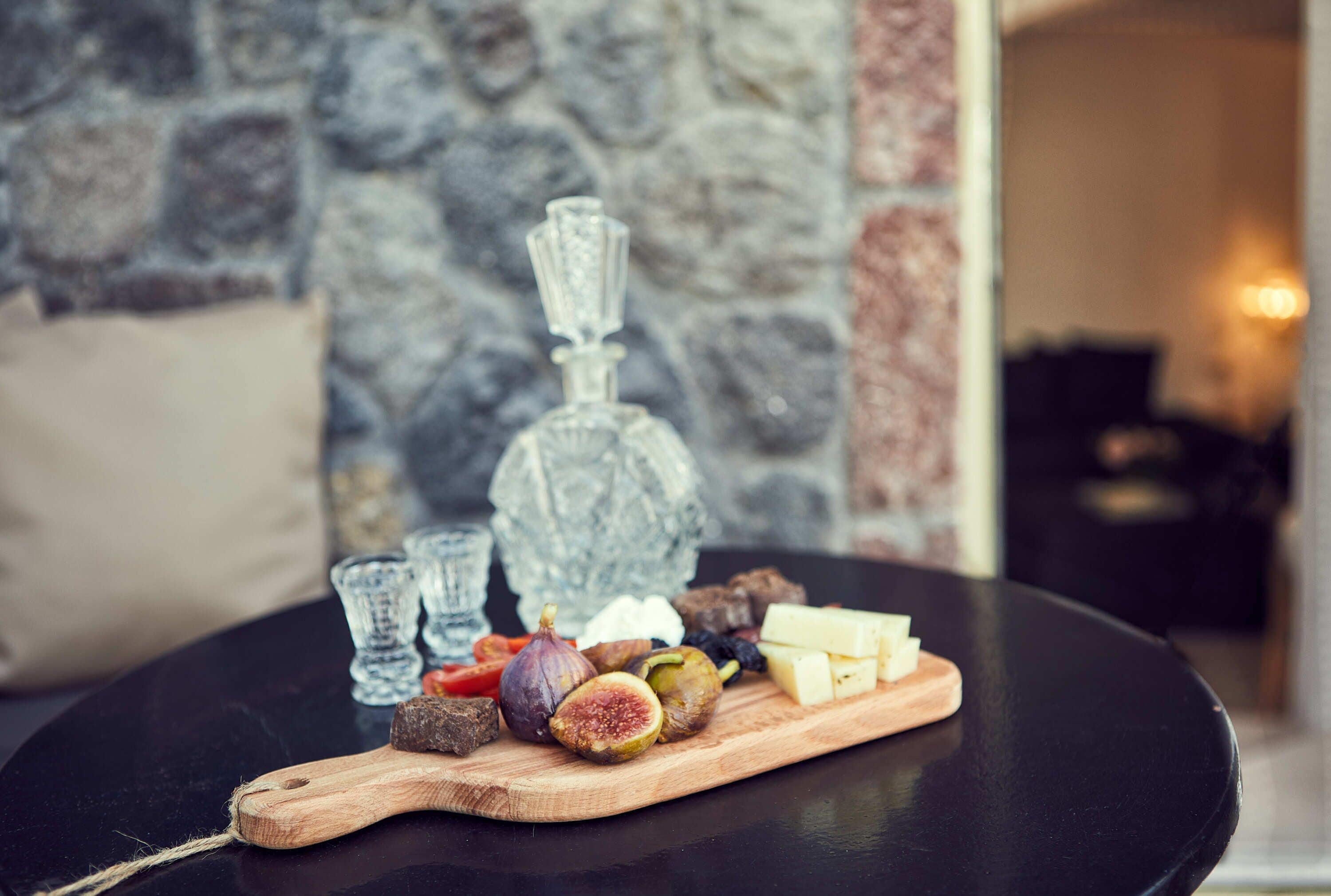 A wooden cutting board with various cheeses, figs, and other items on a black table.