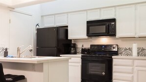 A modern kitchen with white cabinetry, a black refrigerator, a microwave, a coffee maker, and a stove. - Cozy condo near MCC, pool, covered parking (Mesa)