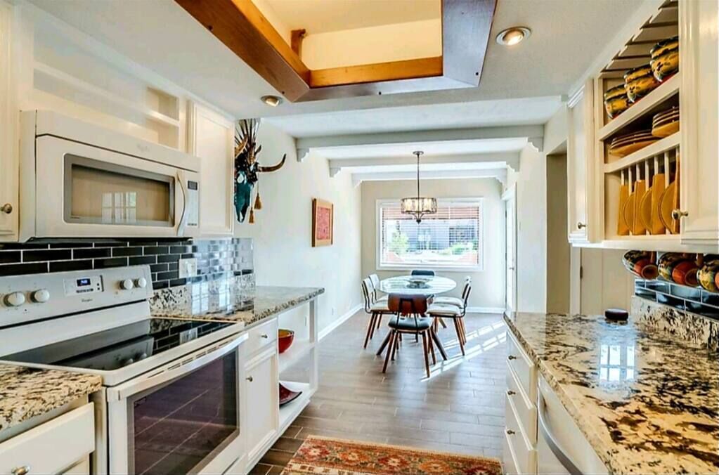 A kitchen with white cabinets, a granite countertop, and a dining area with a table and chairs.