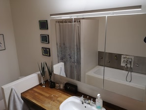 A bathroom with a wooden vanity, a white sink, a mirror, a shower with a beige curtain, and a wall-mounted faucet.