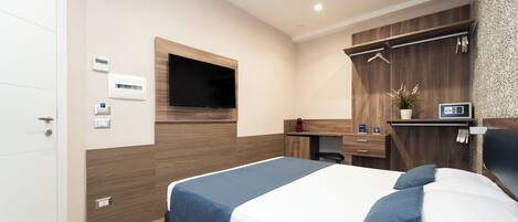 A modern hotel room with a bed, a TV mounted on the wall, a desk, and a wardrobe.