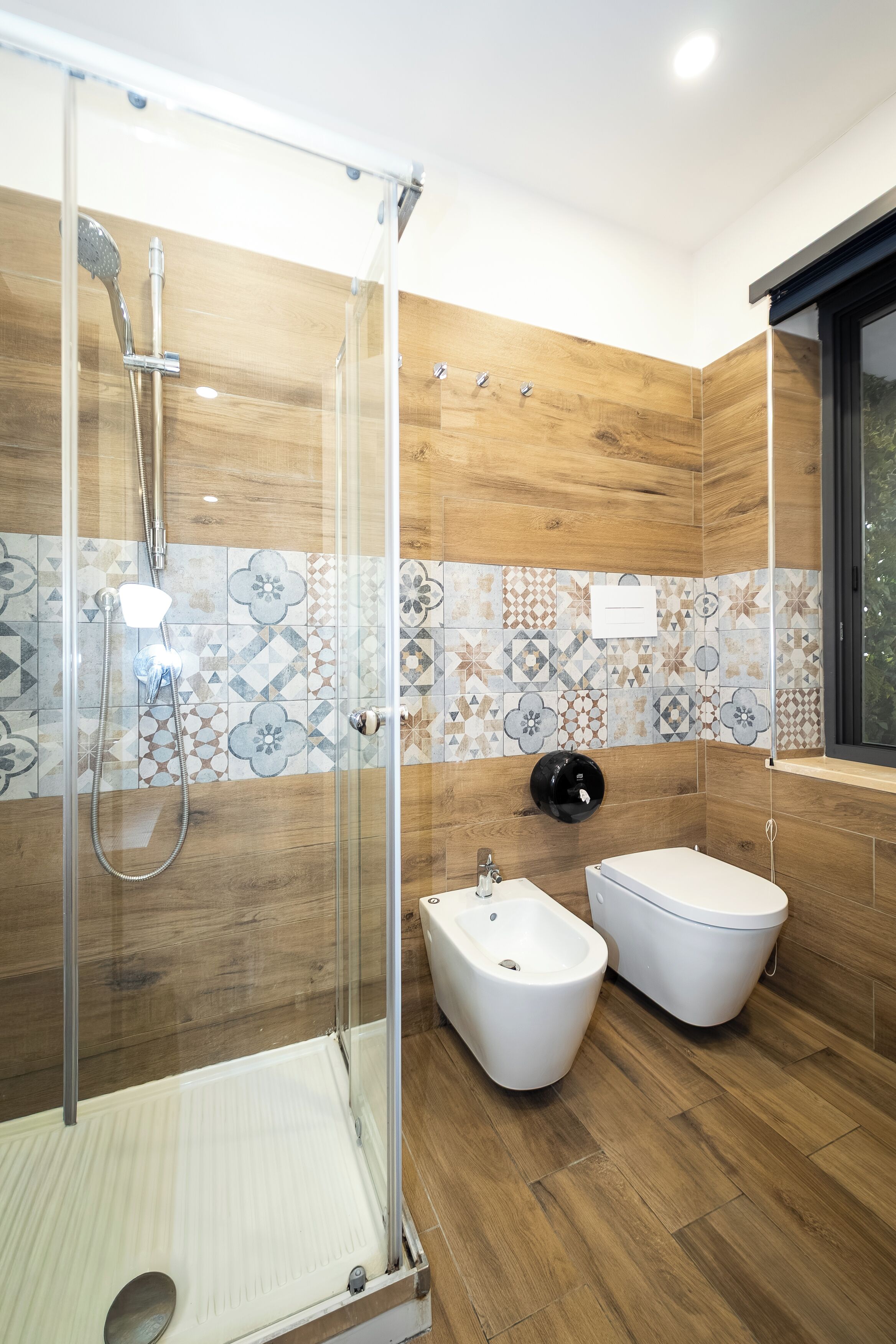 A modern bathroom with a shower enclosure, bidet, and a window.