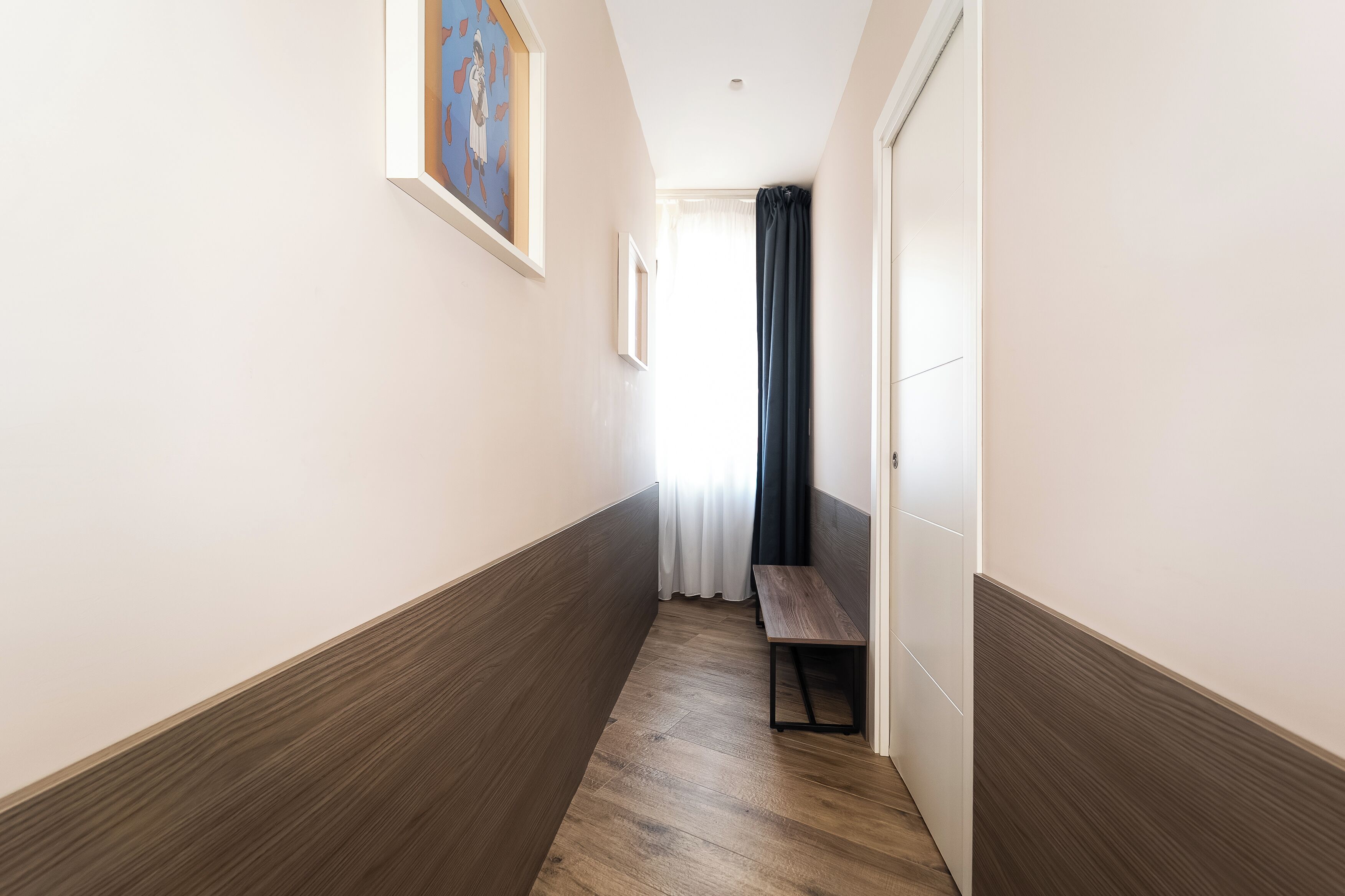 A hallway with wooden flooring, a bench, and a door.