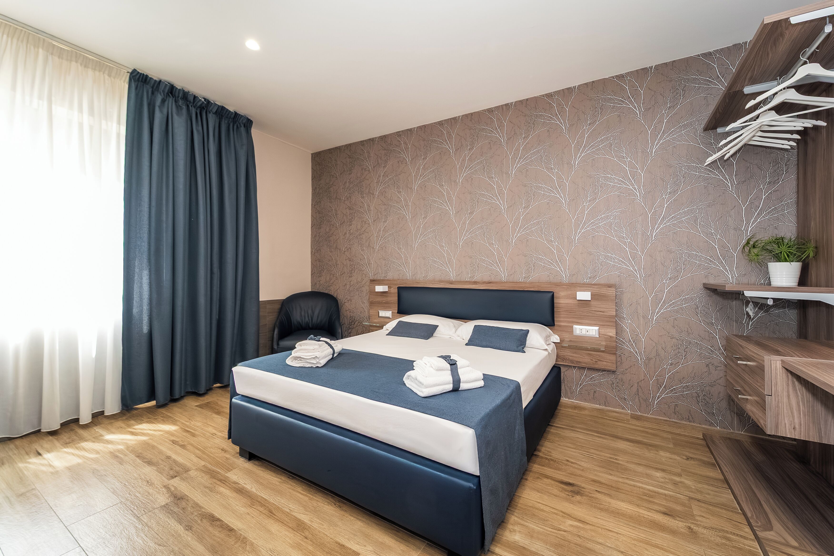 Una habitación de hotel moderna con una cama grande, cabecera de madera, escritorio integrado y una planta en maceta.