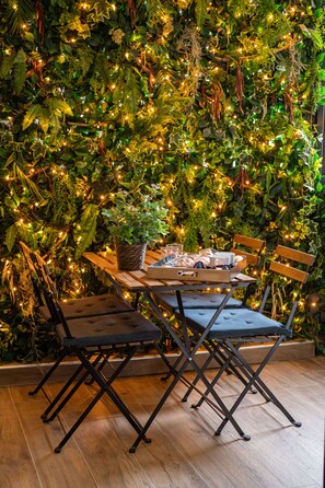 A table set with chairs against a wall of green foliage and string lights.