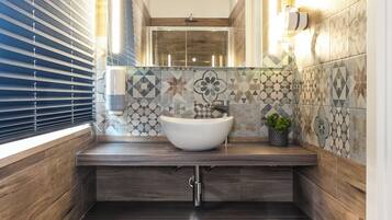 Un bagno stretto con pavimento in legno, un lavandino bianco e una parete di fondo rivestita di piastrelle decorate.